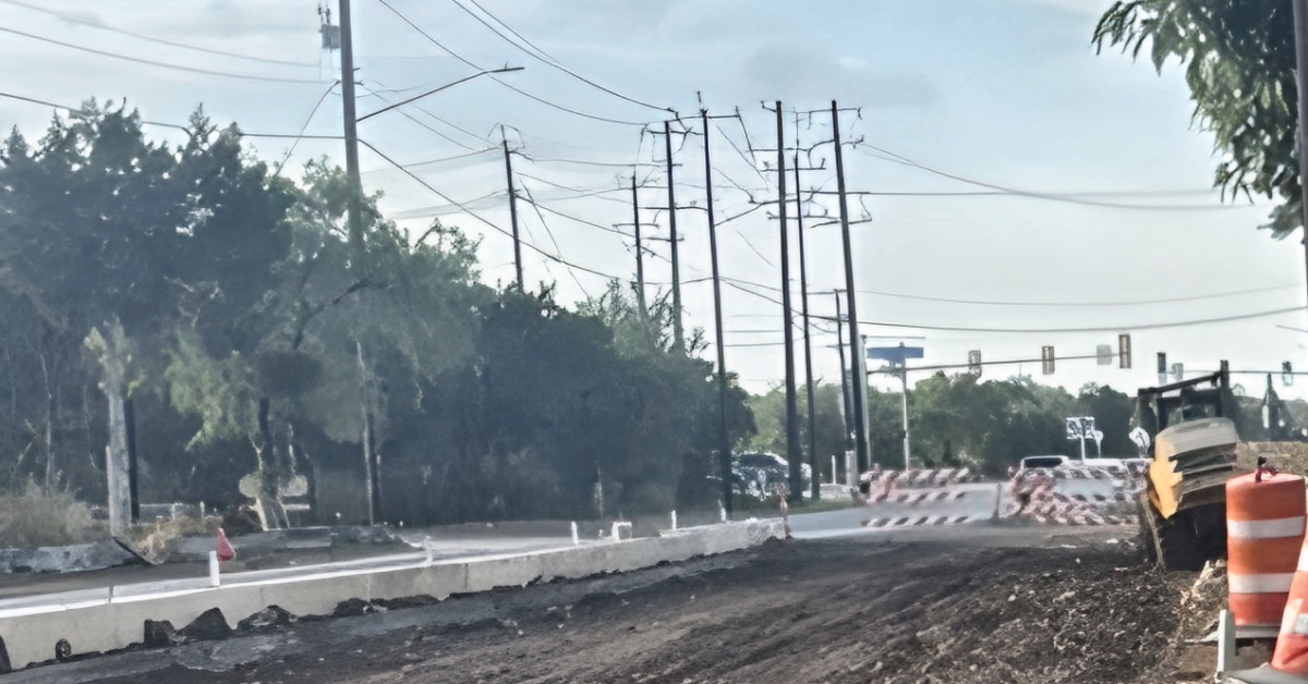 Babcock Road under construction at Hausman Road in Northwest San Antonio, with graded roadbed, new curb, barricades and a loader.